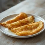 Low Carb Crepes: Golden low carb crepes stacked on a plate with crisp edges and a glistening butter coating.