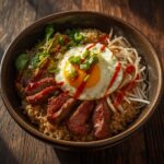 A fresh steak-and-egg fried rice bowl topped with a sunny-side-up egg and green onions on a rustic table.