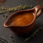 A rich and glossy Keto Gravy Recipe served in a ceramic boat on dark slate