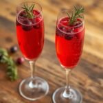 Refreshing Low Carb Cranberry Mimosa served in a flute with fresh cranberries and rosemary garnish