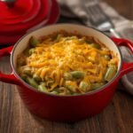 A rustic red pot of bubbling Low Carb Green Bean Casserole on a wooden table.